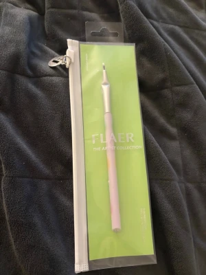 Sminkborste från FLAER Artist Collection - Sminkborste från FLAER The Artist Collection med ett stilrent, metalliskt rosa handtag och silverfärgad borsthållare. Borsten är liten och platt, perfekt för detaljerad applicering av smink. Kommer i en praktisk förvaringspåse.