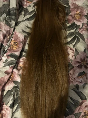 Lång brun hårklämma med löshår - Snygg hårklämma med långt, brunt löshår. Perfekt för att snabbt fixa en fylligare frisyr. Löshåret är rakt och har en naturlig glans. Klämman är diskret och enkel att fästa i håret. Passar dig som vill ha extra volym och längd.