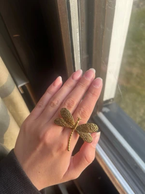 Guldfärgad ring med trollslända - Unik ring i guldfärgad metall med en stor trollslända som motiv. Ringen har detaljerade vingar och kropp som ger en cool och bohemisk känsla. Perfekt för dig som gillar statement-smycken och naturinspirerad design.