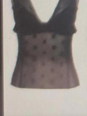Svart mesh topp med prickigt mönster - Snygg svart mesh topp med djup v-ringning och prickigt mönster. Toppen är ärmlös och har en lätt transparent look som ger en trendig vibe. Perfekt att styla med jeans eller kjol för en cool outfit.