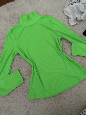 Grön ribbad polotröja - Snygg limegrön ribbad polotröja med lång ärm och figurnära passform. Tröjan har hög krage och är tillverkad i ett stretchigt material som sitter skönt på kroppen. Perfekt för dig som vill sticka ut med färg.