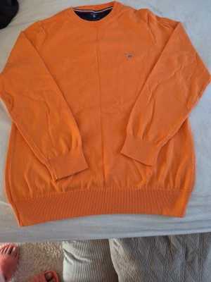 Orange tröja från GANT - Snygg orange tröja från GANT i stretchig bomull. Klassisk rund halsringning med ribbade muddar vid ärmslut och nederkant. Liten GANT-logga broderad på bröstet. Perfekt för dig som vill ha en färgklick i garderoben.