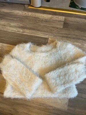 Vit fluffig stickad tröja från H&M - Säljer en vit stickad tröja från H&M med fluffig och mjuk struktur. Tröjan har rund hals och långa ärmar, perfekt för att hålla sig varm under kyliga dagar. Passar storlek xs,s