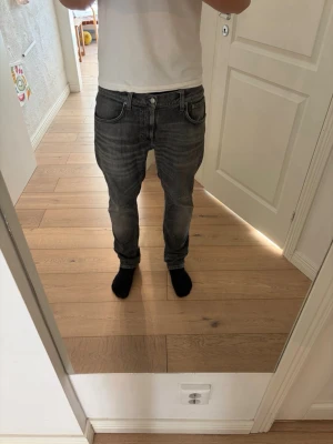 Grå slim fit jeans med tvättad look - Säljer ett par grå slim fit nudie jeans i modellen lean dean, med tvättad look och klassiska fem fickor. Jeansen har normal midja och slimmad passform längs benen. Perfekta för en avslappnad och trendig stil. 