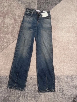 Blå raka jeans från Bershka - Säljer ett par blå jeans från Bershka med raka ben och hög midja. Jeansen har coola sömdetaljer framtill och klassisk femficksdesign. Materialet är denim i bomull och färgen är tvättad blå med lätt slitning. Perfekta för en trendig och avslappnad look.