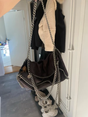 Svart Stella McCartney Falabella väska - Säljer en svart Falabella handväska med silverfärgade kedjedetaljer och axelrem. Och en liten logotypbricka. Köpt utomlands så den är ej ”riktig” så att säga😊 Men sjukt bra kvalitet kedjorna är riktiga och lädertyget jättefint🥰 Enda bristningen är kedjan som jag visar på sista bilden. Går säkert att laga jag hata bara varit för lat att ta tag i det. Uppskattar storleken som Mellan stor den rymmer SÅ mycket men är inte för stor eller för liten (enligt mig)