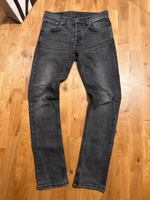 Svarta jeans från Nudie Jeans - Säljer ett par svarta jeans från Nudie Jeans med klassisk femficksmodell och raka ben. Jeansen har en snygg tvättad look och kontrastsömmar. Tillverkade i mjuk denim som sitter skönt och passar till det mesta. Perfekta för dig som gillar stilrena och tidlösa jeans.