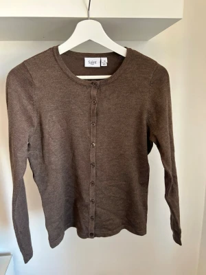 Brun kofta från Saint - Klassisk brun kofta från Saint tropez med rund halsringning och knappar hela vägen framtill. Långärmad och i tunt, mjukt material som passar perfekt till lager på lager. Enkel och stilren design som funkar till det mesta. Storlek Xs, aldrig använd, inga defekter. 🩷🩷🩷