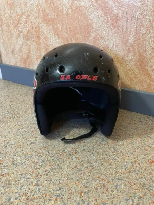 Svart hjälm med röda flames - Cool svart hjälm med röda och vita flames på sidan och ventilationshål upptill. Utrustad med hakrem och mjuk vaddering på insidan för extra komfort. Passar perfekt för skate eller cykel. Unik detalj med röd text framtill.