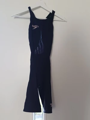 Svart tävlingsbaddräkt från Speedo - Säljer en svart tävlingsbaddräkt från Speedo med ben och breda axelband. Materialet är slätt och snabbtorkande, perfekt för simträning och tävling. Original pris 1300