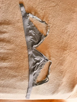 Ljusblå spetsbralette - Snygg ljusgrå bralette i satin med tunna axelband och spetsdetaljer längs kanterna. Triangelkupor utan vaddering och justerbara axelband för perfekt passform. Perfekt för dig som gillar en enkel och stilren look. Endast provad. 