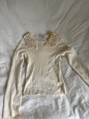 Beige stickad topp med volangkrage - Supersöt benvit långärmad topp med unik volangdetalj runt kragen. Figurnära i passformen. Den är från &other stories och väldigt skönt material. Används 1 gång men väljer att sälja för att den är för liten. 