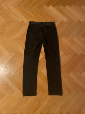 Svarta raka jeans från Nudie jeans, Rad Rufus - Säljer ett par svarta jeans från Nudie Jeans med klassisk femficksmodell och raka ben. Jeansen har normal midja och är tillverkade i ett slitstarkt bomullsmaterial. Perfekta för dig som gillar en tidlös och enkel stil. Man