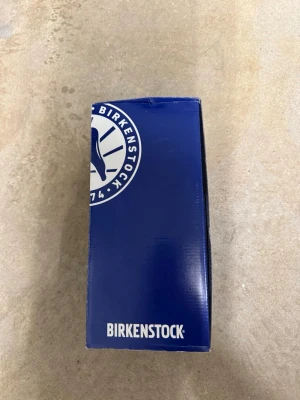 Birkenstock Arizona svarta sandaler - Klassiska Birkenstock Arizona sandaler i svart läder med två justerbara remmar och metallspännen. Fotbädden är i kork och mocka för extra komfort. Perfekta för en avslappnad och trendig stil. Stor i storleken, passar dig som har 42 i normalstorlek.