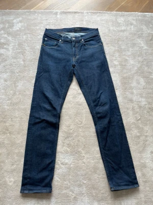 Mörkblå raka jeans från tiger if Sweden - Snygga mörkblå jeans från tiger of Sweden med klassisk femficksmodell och slim ben. Jeansen har en stilren look med diskreta sömmar och patch med logga bak i midjan. Perfekta till en avslappnad men ändå trendig outfit.