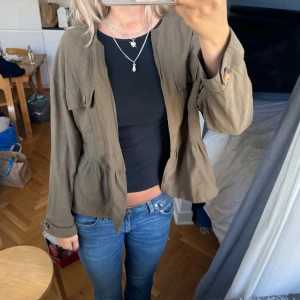 Olivgrön jacka med fickor Zara  - Intressekoll på en olivgrön / militärgrön / khaki tunn jacka med snygga knappar på ärmslut och bröstfickor. Jackan har en loose passform och är tillverkad i mjukt bomullsmaterial. Den har en cool peplum-detalj vid midjan som ger en unik look. Perfekt att slänga över en t-shirt. Slutsåld. 
