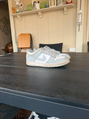 Nike Dunk Low vit/grå sneaker - Nike Dunk Low sneakers i vitt och ljusgrått läder med klassisk Swoosh på sidan. Lågt skaft och perforerad tåbox för extra ventilation. Tidlös och clean design som passar till det mesta. Yttersula i gummi för bra grepp. Man får med snören 
