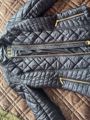 Svart quiltad vindjacka från Barbour - Snygg svart vindjacka från Barbour International med quiltat mönster och guldfärgade dragkedjor. Knappt använd och är i super skick. Storlek 36. Nypris ca 3000/3500.  