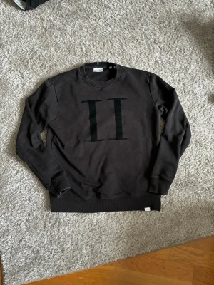 Svart sweatshirt med II-tryck - Cool svart sweatshirt från Les Deux med stort II-tryck på bröstet. Tröjan har rund hals, ribbade muddar och är tillverkad i mjukt bomullsmaterial. Perfekt för dig som gillar stilrena och trendiga plagg.