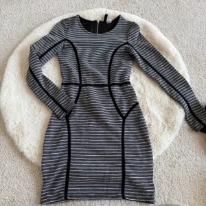 Grå och svart bodycon-klänning H&M - Snygg bodycon-klänning från H&M Divided i grått med svarta ränder och markerade svarta sömmar. Klänningen har lång ärm, rund halsringning och dragkedja i ryggen. Perfekt för dig som gillar en stilren och modern look.