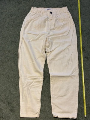 Beige linnebyxor med resårmidja  - Snygga beige linnebyxor med avslappnad passform och resår i midjan. Byxorna har sidfickor fram och knappar bak, vilket ger en stilren look. Perfekta för en chill och trendig stil. Materialet är lätt och luftigt linne. De är sjukt bra skick ser knappast att de är använda men om man har funderingar så är det bara att säga till så försöker jag lösa de så snabbt som möjligt.  Priset är ej hugget i sten. 