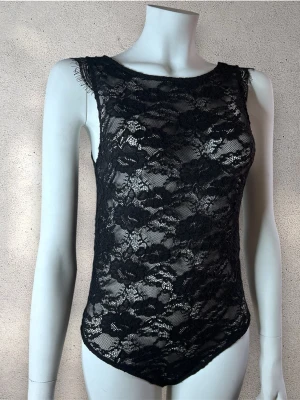 Svart spetsbody med blommönster - Snygg svart body i transparent spets med blommigt mönster. Ärmlös modell med rund halsringning och fina spetsdetaljer. Perfekt för dig som vill ha en trendig och elegant look. #sainttropez