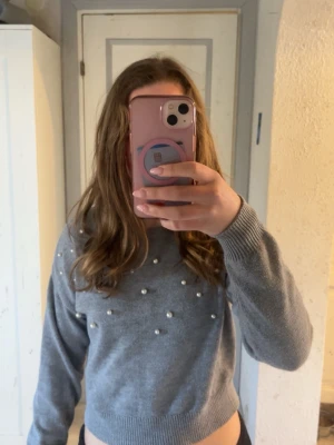 Grå stickad tröja med pärlor - Snygg grå stickad tröja med dekorativa pärlor framtill. Tröjan har rund halsringning, långa ärmar och ribbade muddar vid ärmslut och nederkant. Perfekt för dig som vill ha en trendig och mysig look🩶Kolla in min profil för fler fina och trendiga plagg!