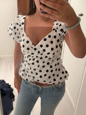 Vit prickig omlottblus med puffärm - Säljer en vit omlottblus med svarta prickar och puffiga korta ärmar. Blusen har v-ringning och markerad midja som ger en snygg siluett. Perfekt för dig som gillar trendiga och lekfulla toppar! Ifrån dorothy perkins, st L men passar mer S /Xs Har en liten defekt vid dragkedjan men inget som syns/ störs.