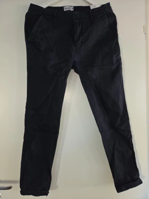 Svarta chinos från Mouli - Snygga svarta chinos från Mouli med klassisk passform och raka ben. Byxorna har två snedställda fickor fram och är tillverkade i ett mjukt bomullsmaterial som är bekvämt att bära. Perfekta för dig som vill ha en stilren look.