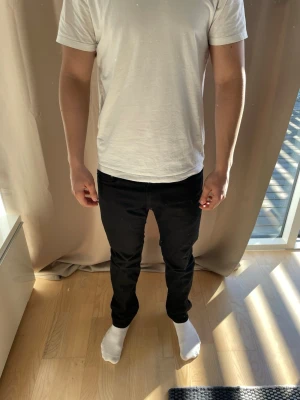 Svarta slim fit jeans herr - Säljer ett par svarta slim fit jeans med klassisk femficksdesign och normal midja. Jeansen har smal passform hela vägen ner och är tillverkade i ett stretchigt material för extra komfort. Perfekta till en avslappnad och stilren look.