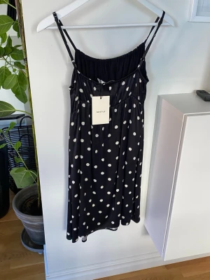 Svart prickig klänning Gestuz - Ny med prislapp - Svart midilång klänning från Gestuz med vita prickar och tunna axelband. Klänningen har en smockad överdel och ett ledigt fall. Fodrad / underkjol