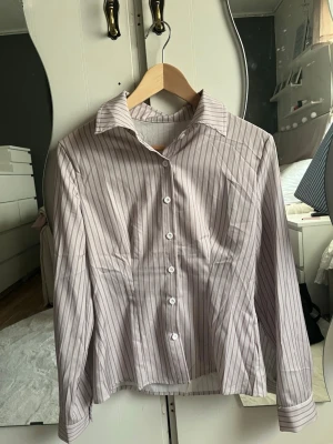 Randig vit skjorta med knappar - Säljer en figursydd skjorta i en beige färg. Skjortan har lång ärm, krage och knäppning framtill med vita knappar. Passar även en storlek S