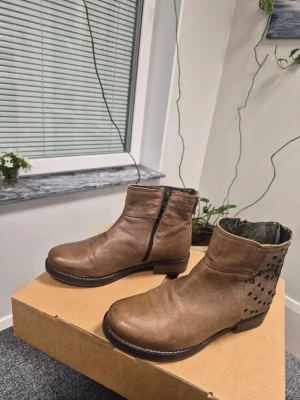 Bruna löder stövletter med detaljerad nitar från Dasia 36 - Snygga bruna stövletter i läder med låg klack och dragkedja på sidan. Baksidan är dekorerad med coola nitar som ger ett trendigt uttryck. Perfekta för dig som vill ha en stilren men edgy look.