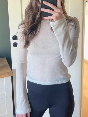 Beige mesh långärmad topp - Säljer en tunn, vit mesh topp med långa ärmar och rund hals. Toppen är lätt transparent och har en slim fit passform som sitter snyggt på kroppen. Perfekt att styla lager på lager eller med ett linne under.