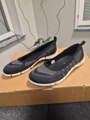 Nya Svarta stickade ballerinas från Ecco super bekväma 36 38 - Snygga svarta ballerina skor från Ecco med stickad ovandel och vit, mönstrad sula. Skorna har en sportig design med diskreta detaljer och en praktisk flik bak. Blev fel vid köpet och fick två olika storlekar 36 38. Perfekt för dig som gillar både komfort och stil.
