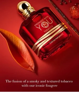 Stronger With You Tobacco parfym - En elegant parfymflaska i djup röd färg med gulddetalj. Flaskan har rundade former och texten 'Stronger With You Tobacco' på framsidan. Doften beskrivs som en fusion av rökig och texturerad tobak med fougère.