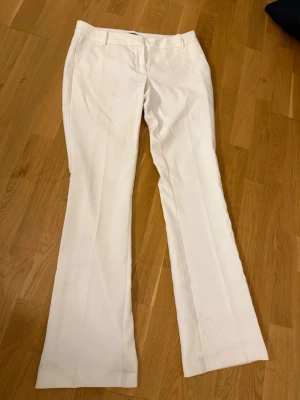Vita kostymbyxor med pressveck - Snygga vita kostymbyxor med klassiskt pressveck och raka ben. Byxorna har hällor för bälte och diskret stängning framtill. Perfekta för dig som vill ha en clean och stilren look. Materialet känns lätt och bekvämt.