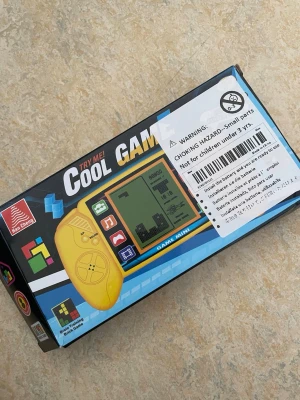 Blå Game Mini retro spelkonsol - Säljer en blå Game Mini retro spelkonsol från Han Cheng. Konsolen har en rektangulär form med knappar på sidorna och en LCD-skärm i mitten. Perfekt för klassiska spel som Tetris och Snake. Tillverkad i plast och smidig att ta med sig överallt.