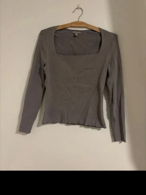 Grå ribbad långärmad topp - Snygg grå ribbad topp med lång ärm och fyrkantig ringning. Toppen har en slim passform med enkel och stilren design.