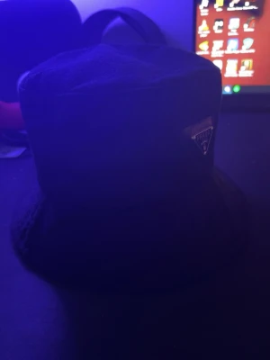 Svart bucket hat från Prada - Stilren svart bucket hat från Prada med klassisk form och diskret logga framtill. Hatten är tillverkad i ett mjukt tygmaterial och passar perfekt för en trendig streetwear-look.