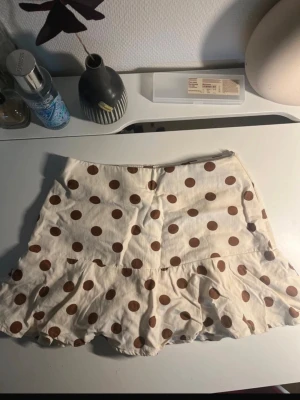 Prickig kjol i beige och brun zara - Supersöt kort kjol med volangkant i beige med bruna prickar. Kjolen har en figurnära passform upptill och en volang nedtill som ger en lekfull look. Perfekt för dig som gillar trendiga och unika plagg.