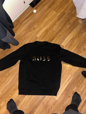 BOSS sweatshirt Xxl men passar xl bra - Cool svart sweatshirt från BOSS med stort, glansigt logotryck på bröstet. Tröjan har rund hals och långa ärmar, perfekt för en avslappnad och stilren look. Materialet är mjukt och bekvämt, idealiskt för att chilla eller hänga med kompisar.