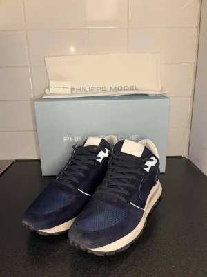 Philippe Model TKLU - Stilrena sneakers från Philippe Model i marinblått. Använda men i gott skick med normalt slitage på sulan, se bild 3. Klassisk modell av hög kvalitet som upplevs något stor i storleken. Perfekt nu under vinter, men funkar även under varmare dagar. Box finns även. Nypris ca 3 200 kr. Vårat pris 1 599kr, 100 äkta. Öppen för seriösa bud. 