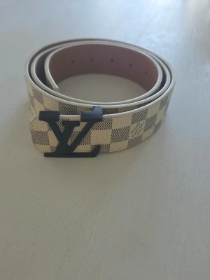 Rutig skärp med spänne - Säljer ett snyggt rutig skärp med klassiskt spänne i svart. Skärpet är beige och grått med rutigt mönster och tillverkat i Perfekt för att lyfta din outfit med en exklusiv touch.