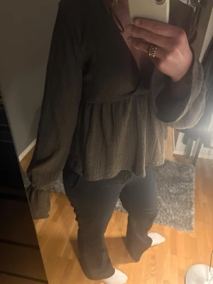 Blus/topp Gina - Säljer jättefin blus med v-ringning och volang nedtill. Blusen har långärmade, vida ärmar och är gjord i ett mjukt, strukturerat tyg som ger en avslappnad men ändå stilren look. Använd ca 3 gånger säljer då den inte längre kommer till användning 