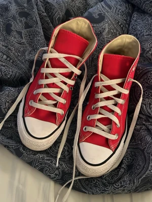 Röda Converse Chuck Taylor sneakers - Klassiska röda Converse Chuck Taylor All Star high-top sneakers med vita snören och tåhätta. Skorna har vit sula med svart rand och är tillverkade i canvas med gummidetaljer. Perfekta för en cool och avslappnad stil. Jag har precis gjort rent dem så de ser ganska nya ut. Ni får gärna lägga bud!