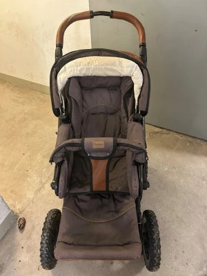 Brun Emmaljunga barnvagn med stora hjul - Säljer en brun barnvagn från Emmaljunga med robusta lufthjul, justerbart handtag i brunt konstläder och rymlig sittdel. Vagnen har sufflett och vadderad insida i beige och brunt tyg. Perfekt för promenader i alla väder.