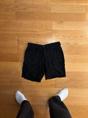 Svarta shorts från Jack and Jones - Svarta shorts med klassisk passform och flera fickor både fram och bak. Stängs med knapp och dragkedja. Perfekta för sommaren och enkla att matcha med olika outfits. 