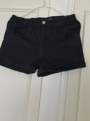 Svarta jeans shorts med uppvik - Snygga svarta jeans shorts med uppvikta benslut och klassisk femficksdesign. Stängs med knapp och dragkedja framtill. Perfekta till sommaren och passar till det mesta. Gjorda i mjuk bomull för skön känsla.