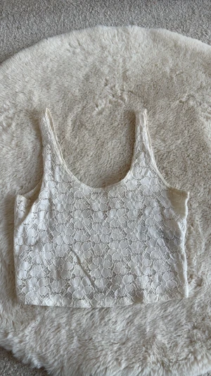 Vit spets-linnetopp från Hollister - Säljer en vit linnetopp från Hollister i storlek XS. Toppen är täckt med blommig spets och har breda axelband. Perfekt för dig som gillar en romantisk och feminin stil.